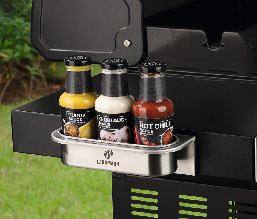 Drei Saucenflaschen (Curry, Knoblauch und Hot Chili) in einem magnetischen Landmann-Edelstahlhalter, der an einem schwarzen Grill befestigt ist.