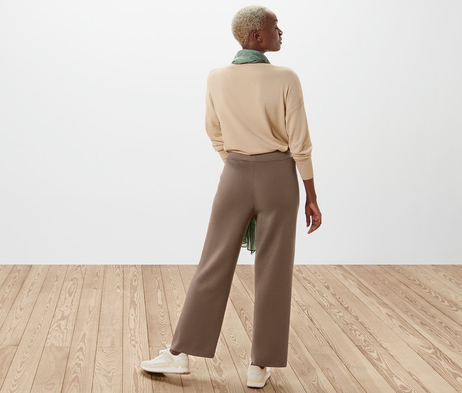 Frau von hinten trägt beigen Pullover und braune Strickhose.