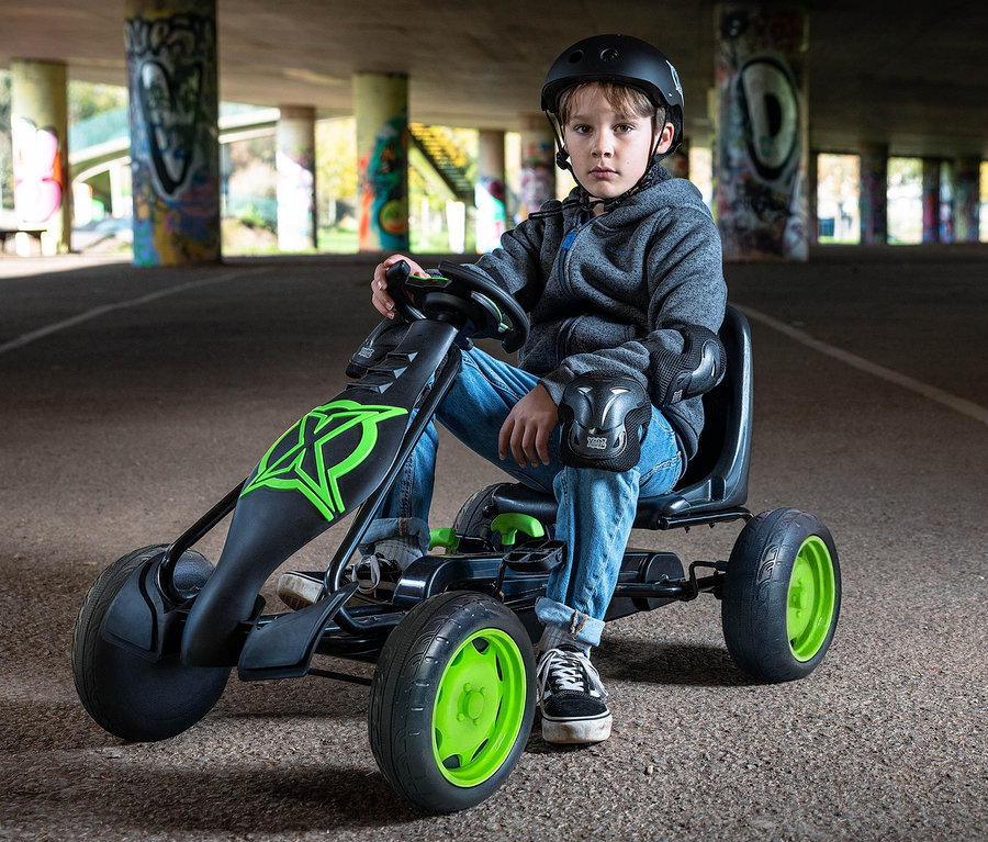 Ein Junge mit Helm und Schützern sitzt auf einem grünen Xootz Gokart »Viper« unter einer Brücke.