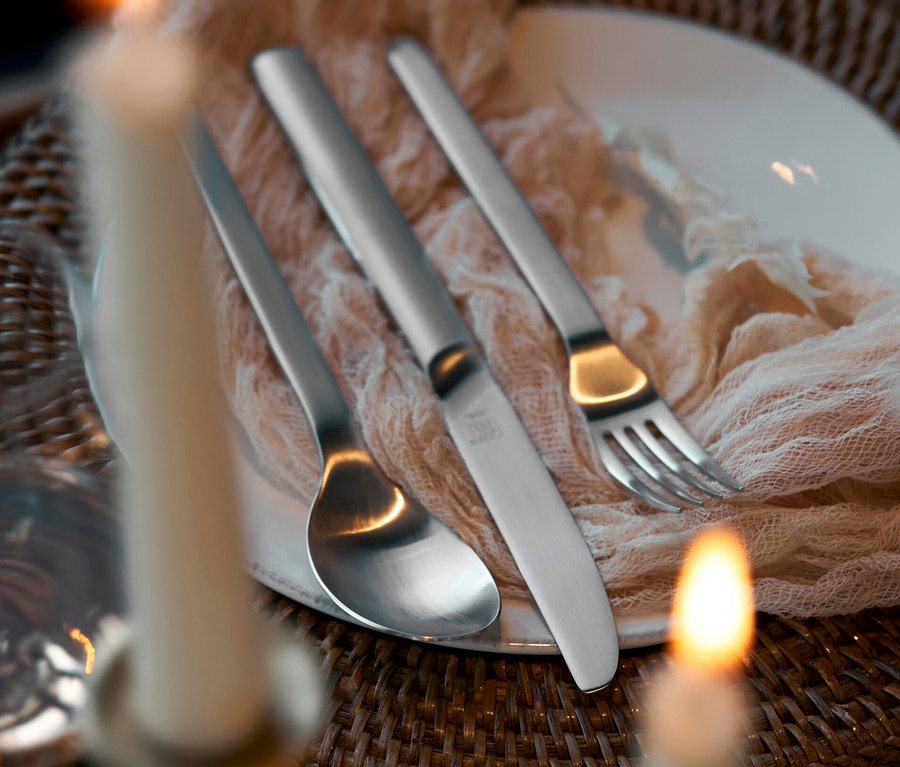 Ein gedeckter Tisch mit einem Teller, auf dem ein Löffel, ein Messer und eine Gabel des ZWILLING Besteck, mattiert, 60-teilig liegen.