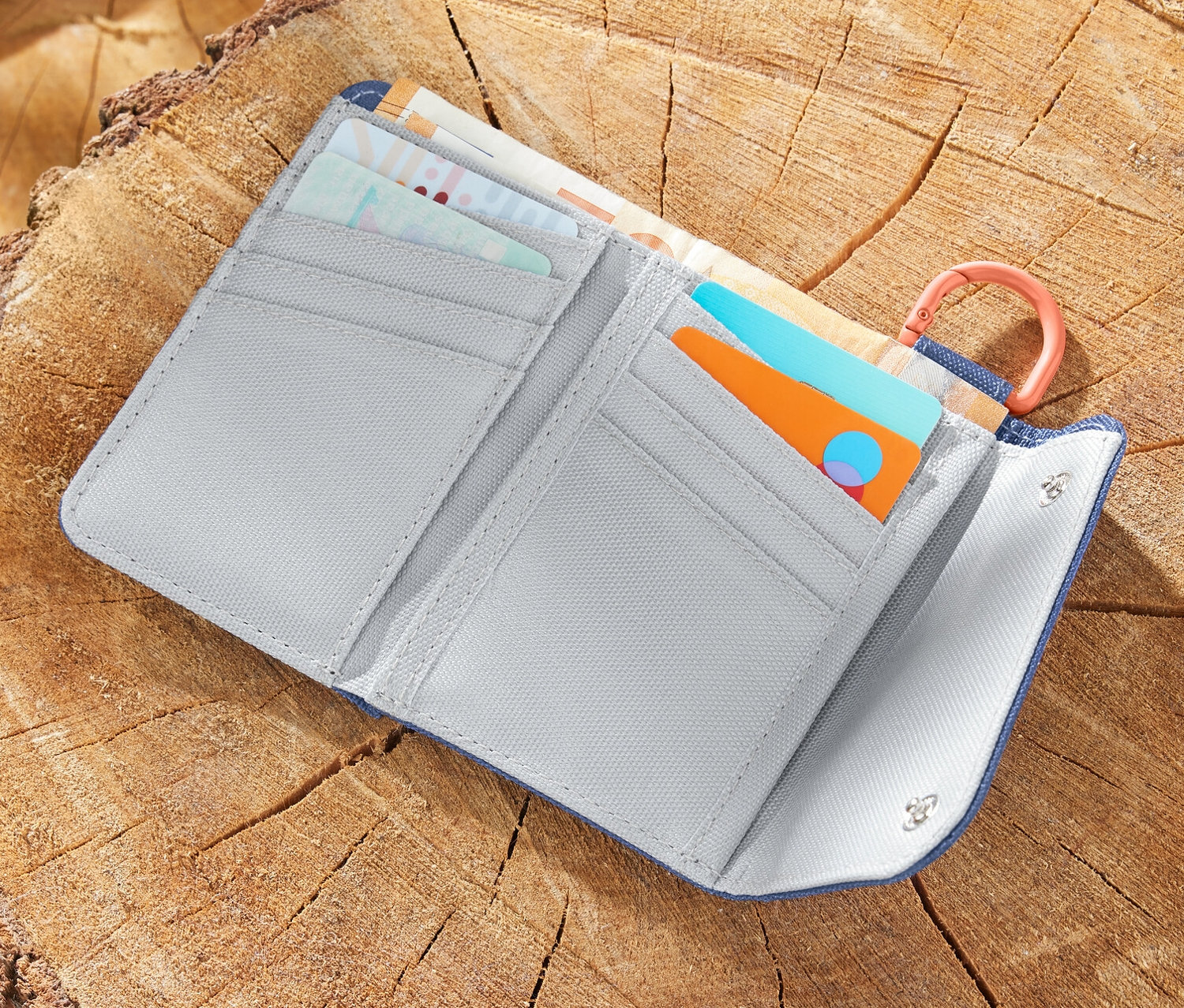 Eine geöffnete Outdoor-Geldbörse liegt auf einem Baumstumpf neben einer Karte und einem Apfel.