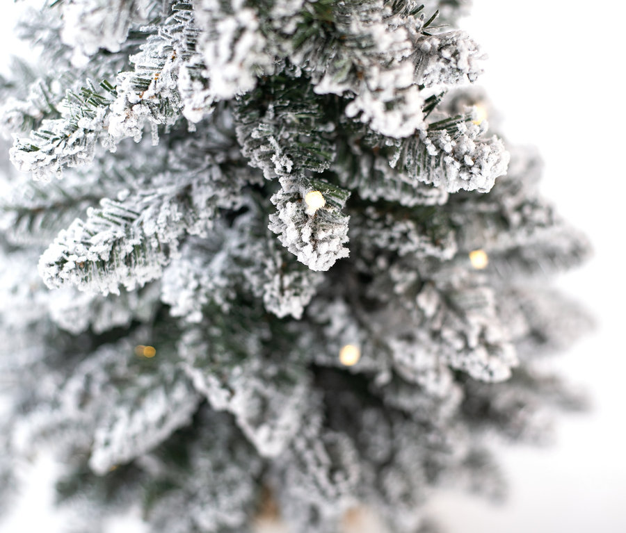 Nahaufnahme eines schneebedeckten Evergreen LED-Weihnachtsbaums mit Jutetopf.