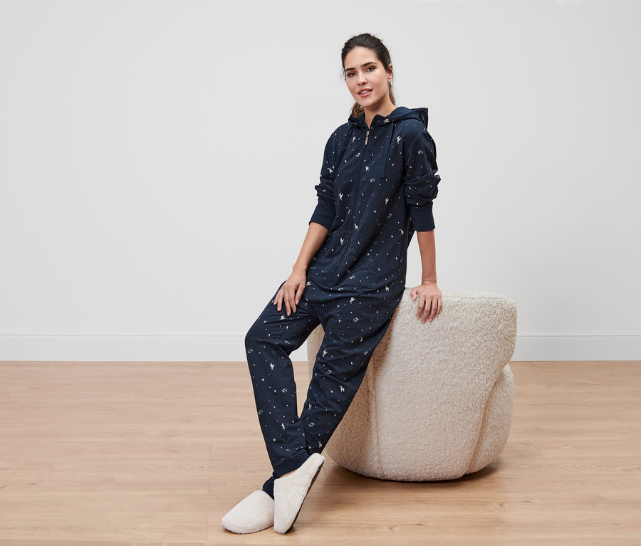 Frau sitzt auf einem Hocker und trägt einen marineblauen Loungeoverall mit Kapuze.