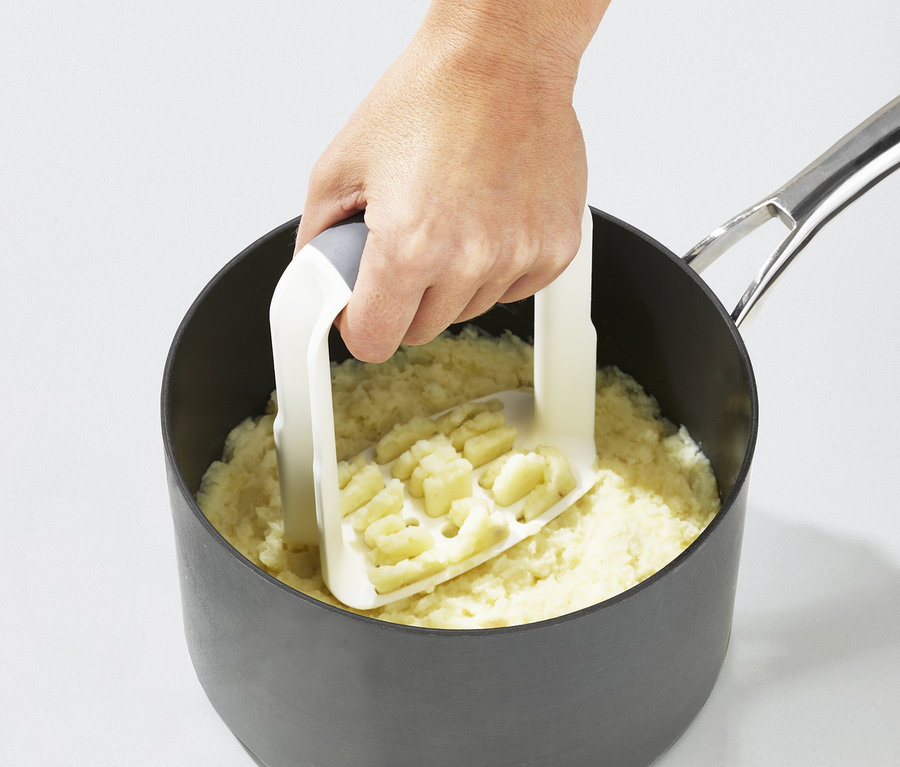 Eine Hand hält einen weißen Joseph Joseph Kartoffelstampfer »Easy-Mash« in einem Topf mit Kartoffelpüree.
