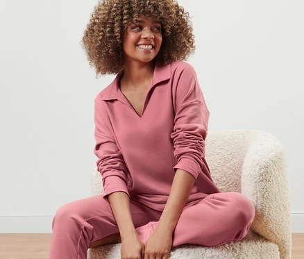 Frau sitzt auf einem Sessel und trägt ein rosenholzfarbenes Lounge-Sweatshirt.