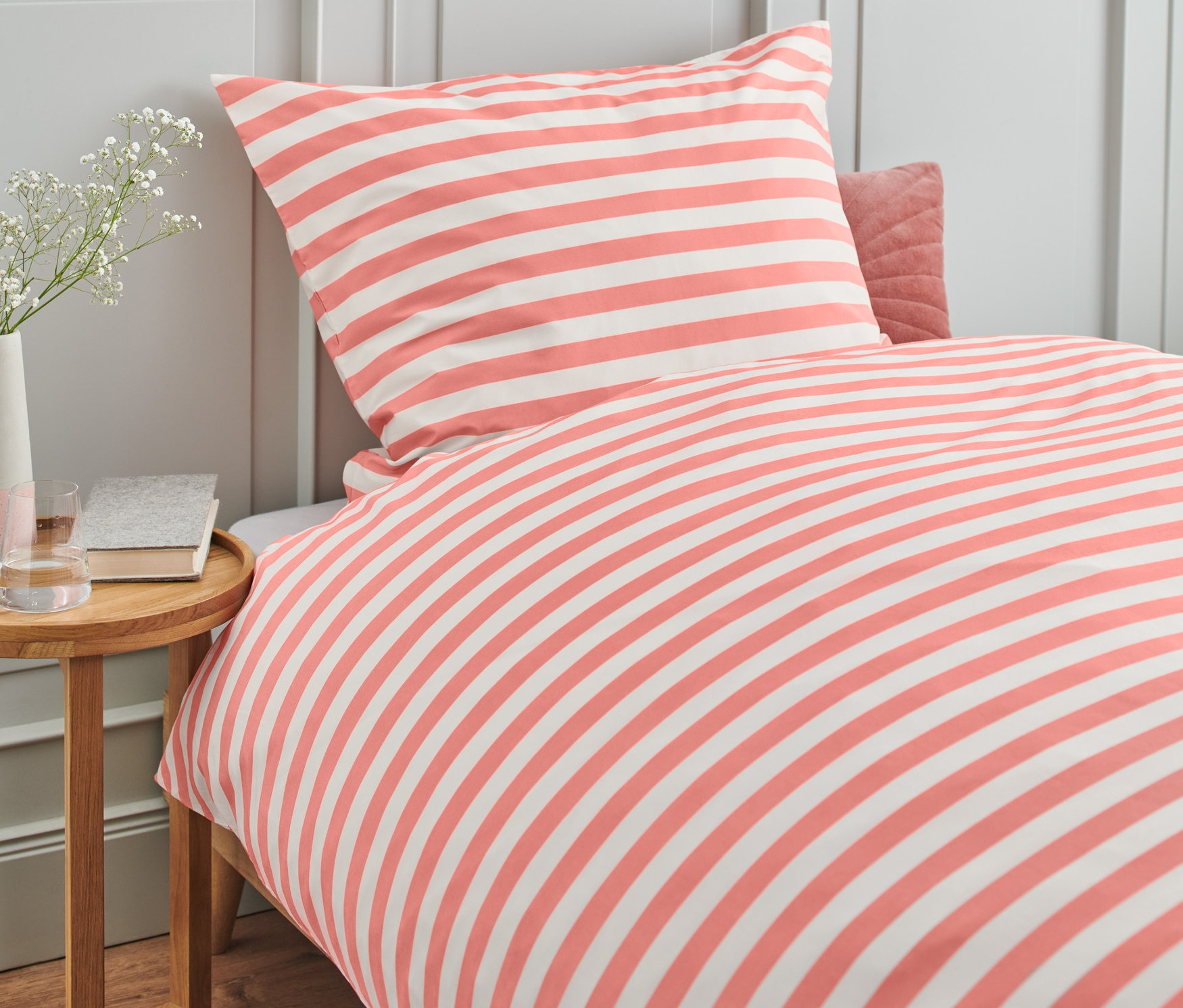 Ein Bett mit rosa-weiß gestreifter Bettwäsche. Premium-Baumwoll-Bettwäsche, Normalgröße.