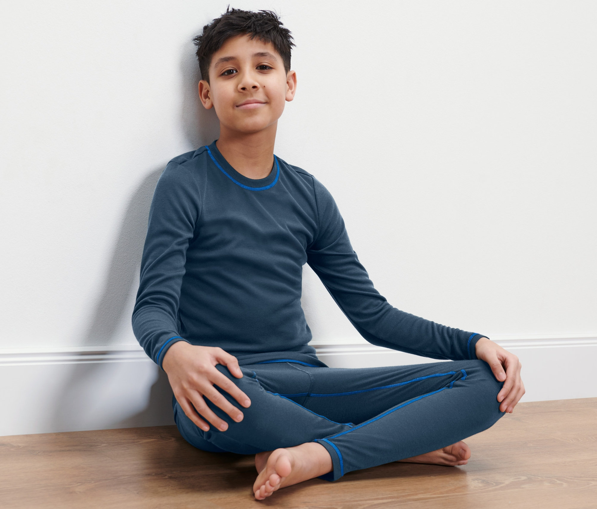 Junge sitzt im Kinder-Ski-und-Winterunterwäsche auf dem Boden.
