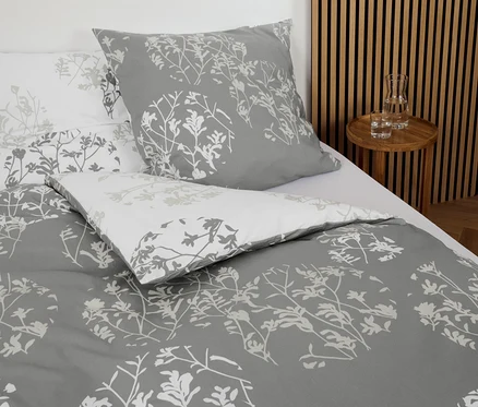 Graue Renforcé-Bettwäsche mit Blumenmuster auf einem Bett.