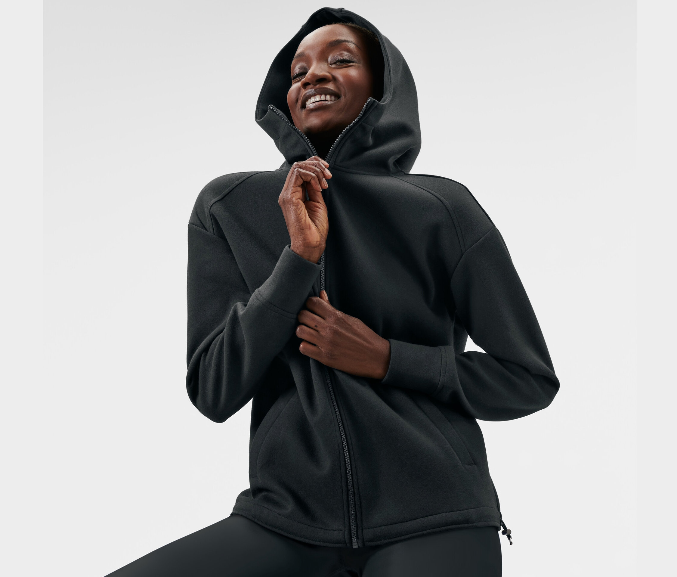Frau schließt eine schwarze Kapuzen-Sweatjacke.