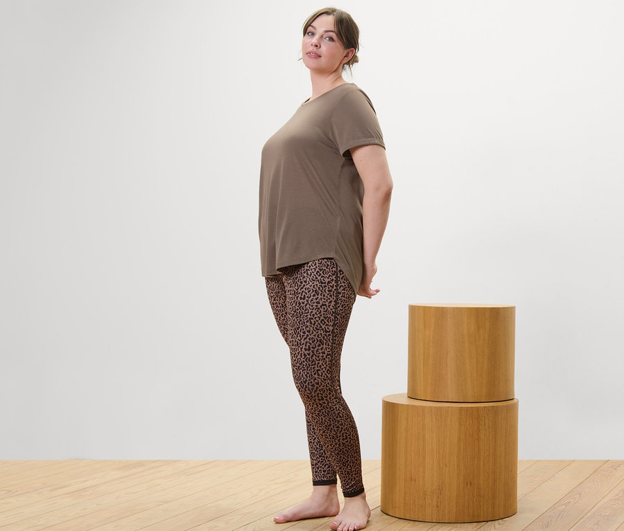Eine Frau steht seitlich und trägt ein taupefarbenes Longshirt und eine dunkelbraun/taupefarbene Wende-Sporttight.