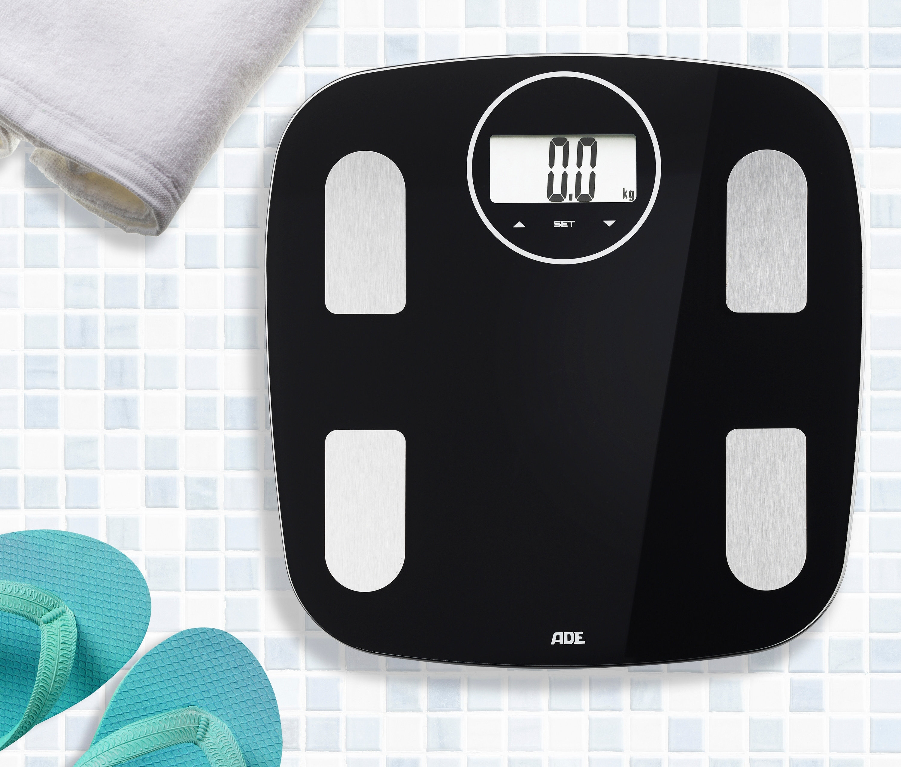 Schwarze digitale ADE Körperanalysewaage auf Fliesenboden mit Handtuch und Flip-Flops.