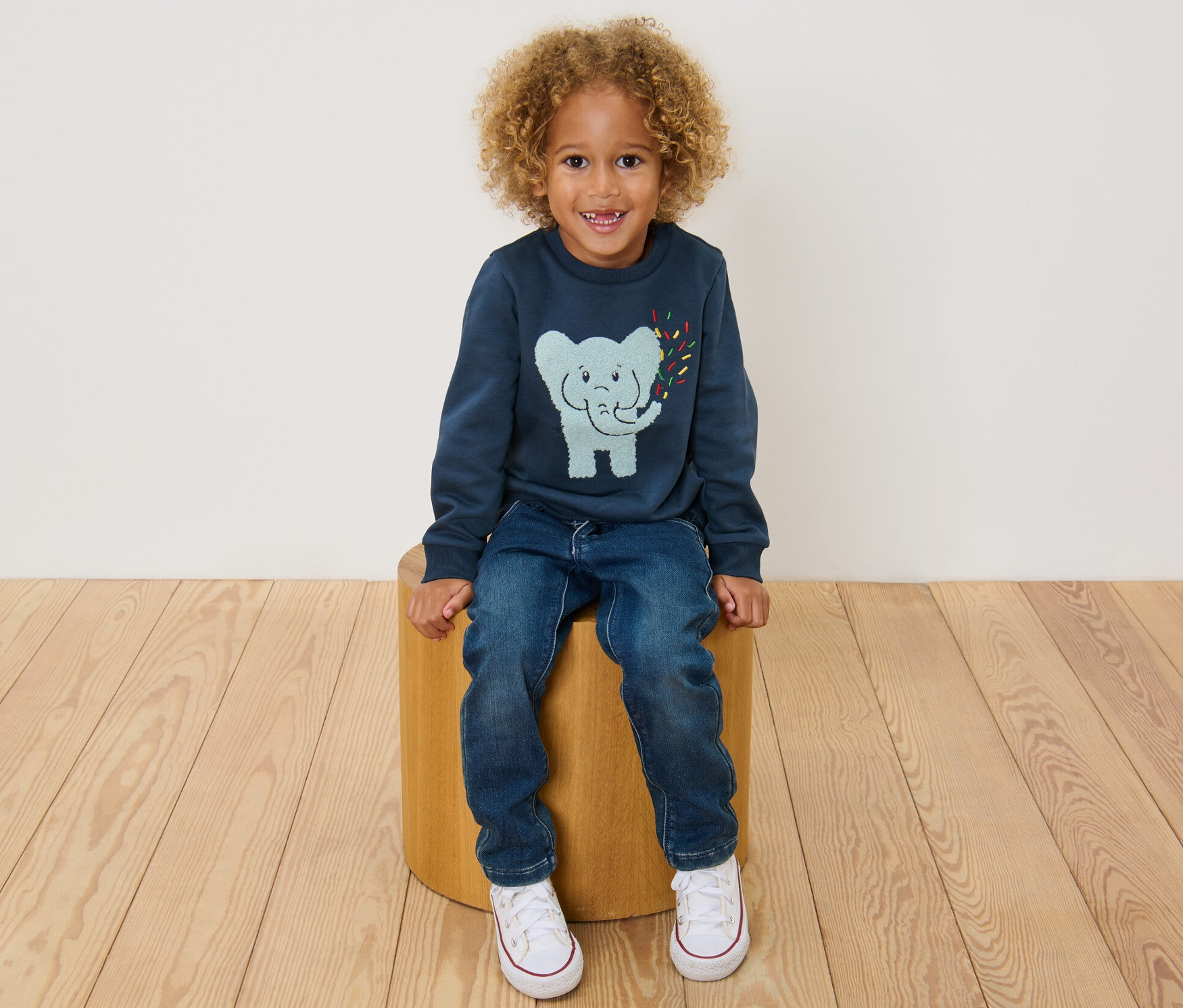 Ein Junge sitzt auf einem Hocker und trägt ein blaues Kinder-Sweatshirt mit angerauter Innenseite.