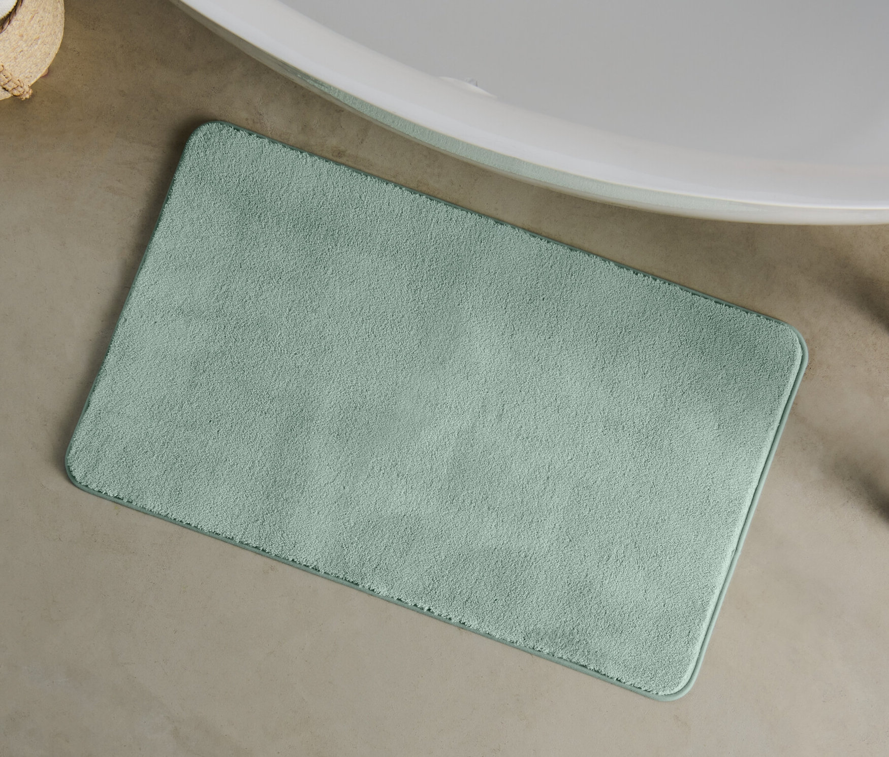 Eine grüne Badematte, ca. 100 x 60 cm, liegt auf dem Boden neben einer Badewanne.