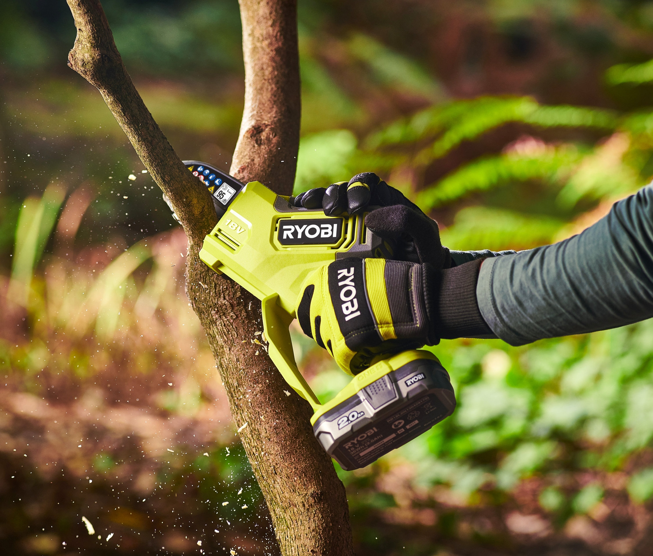 Eine Person sägt einen Ast mit einer RYOBI 18 V One+ Brushless Akku-Einhand-Kettensäge.