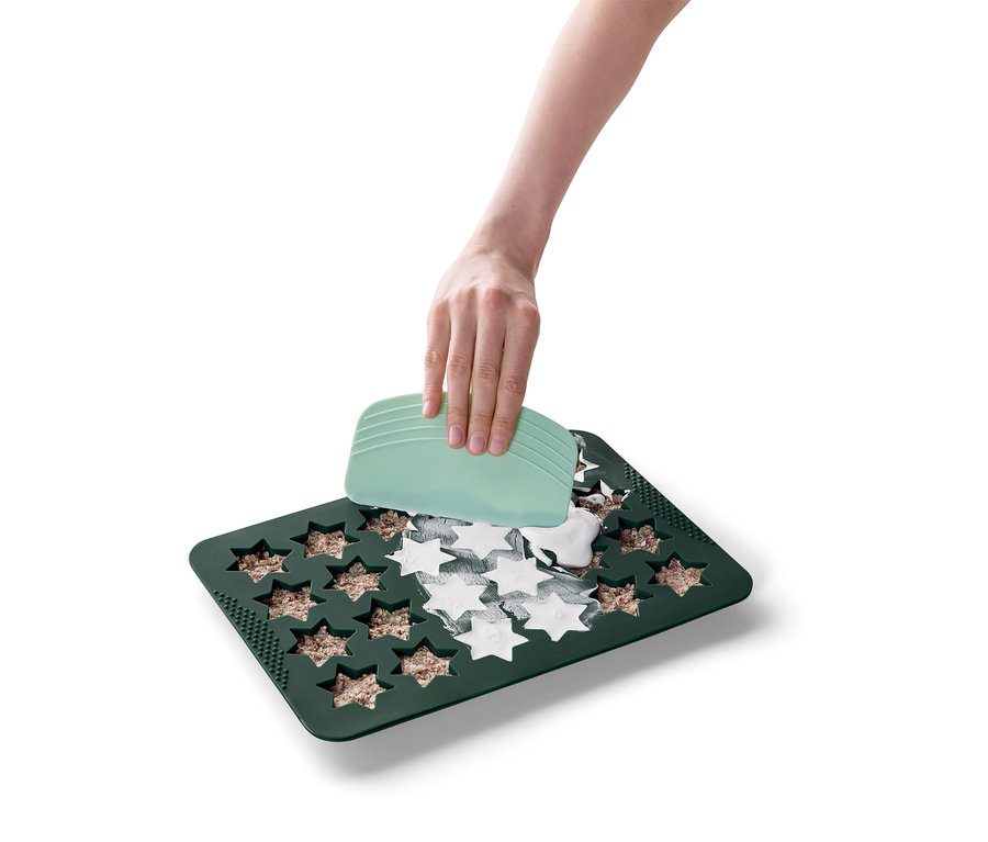 Eine Hand benutzt einen grünen Spatel, um eine weiße Masse in einer grünen sternförmigen Backform zu verteilen.