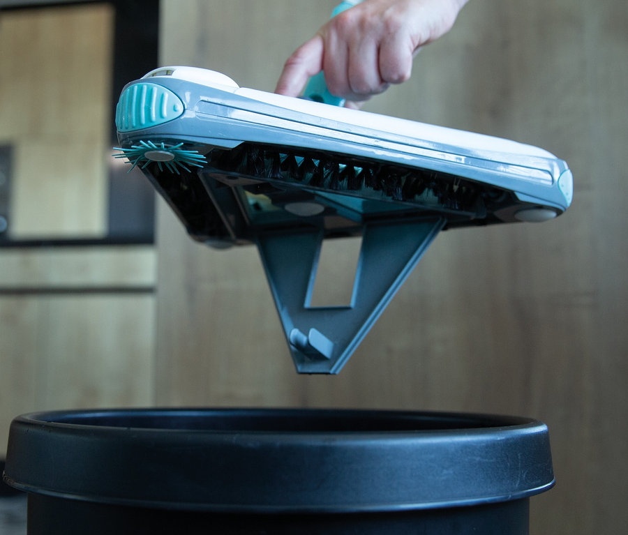 Eine Hand hält einen Akkubesen über einen schwarzen Mülleimer.