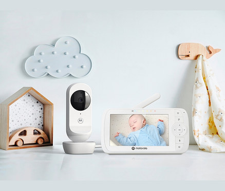 Video-Babyphone »VM34« auf einem weißen Tisch neben Holzspielzeug und Dekorationen.