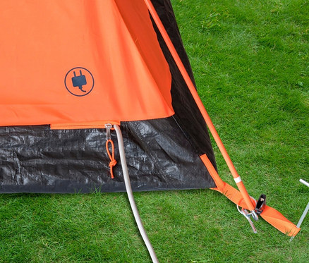 Detailansicht eines orangefarbenen Tambu HAIKA 2 2-Personen-Kuppelzelts mit schwarzem Unterteil und Hering auf Rasen.