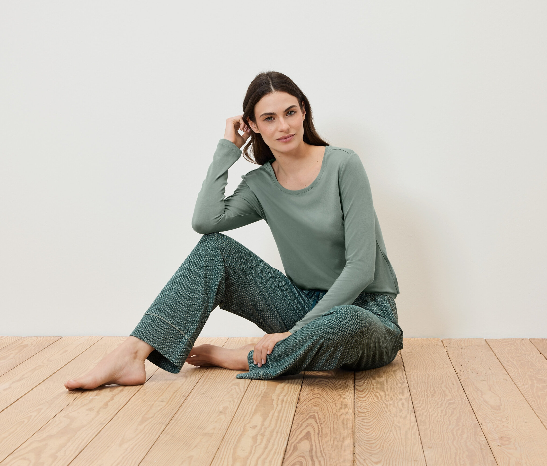 Frau sitzt auf einem Holzboden und trägt einen grünen Pyjama.