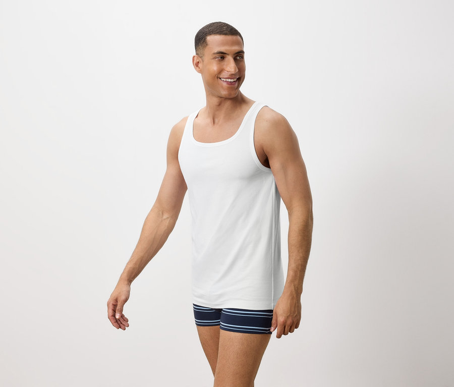 Mann lächelt und trägt ein weißes Tanktop und blaue gestreifte Boxershorts.