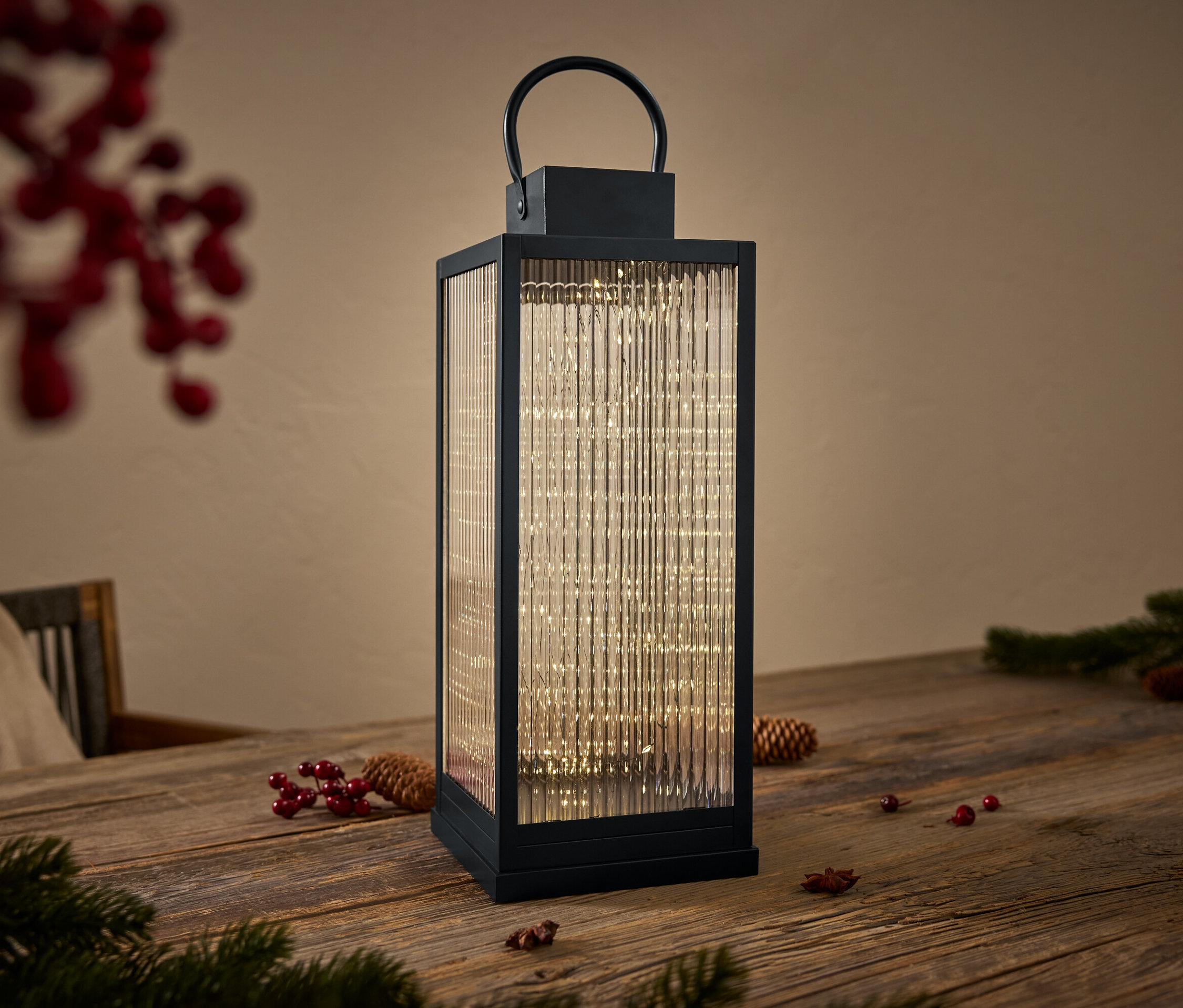 Eine schwarze Laterne mit Glaswänden und Lichtern im Inneren steht auf einem Holztisch.