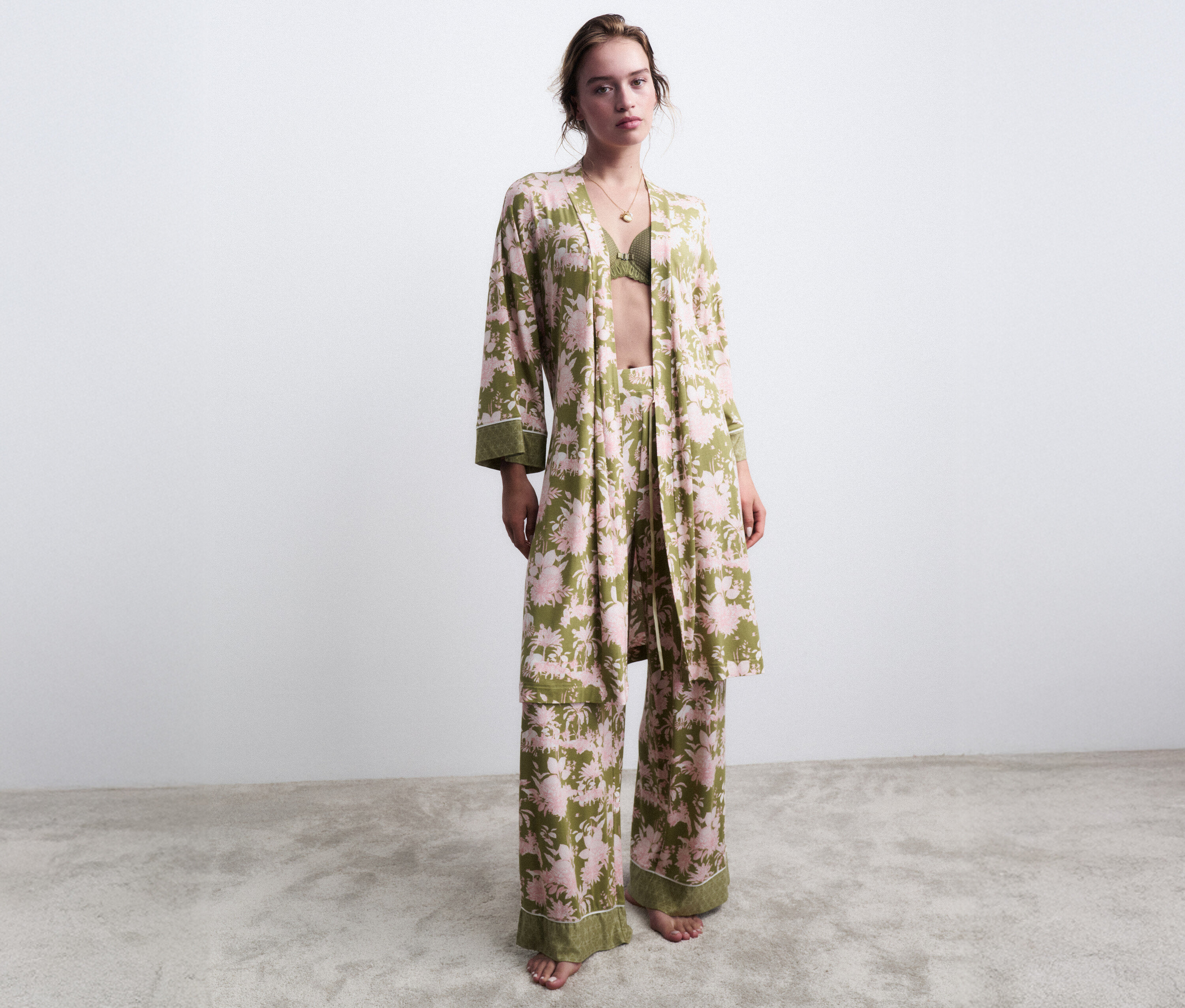 Frau steht barfuß in einem grünen, blumenverzierten Pyjama mit passendem Morgenmantel.