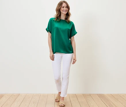Frau trägt ein Blusenshirt im Materialmix in Aqua und weiße Hosen.