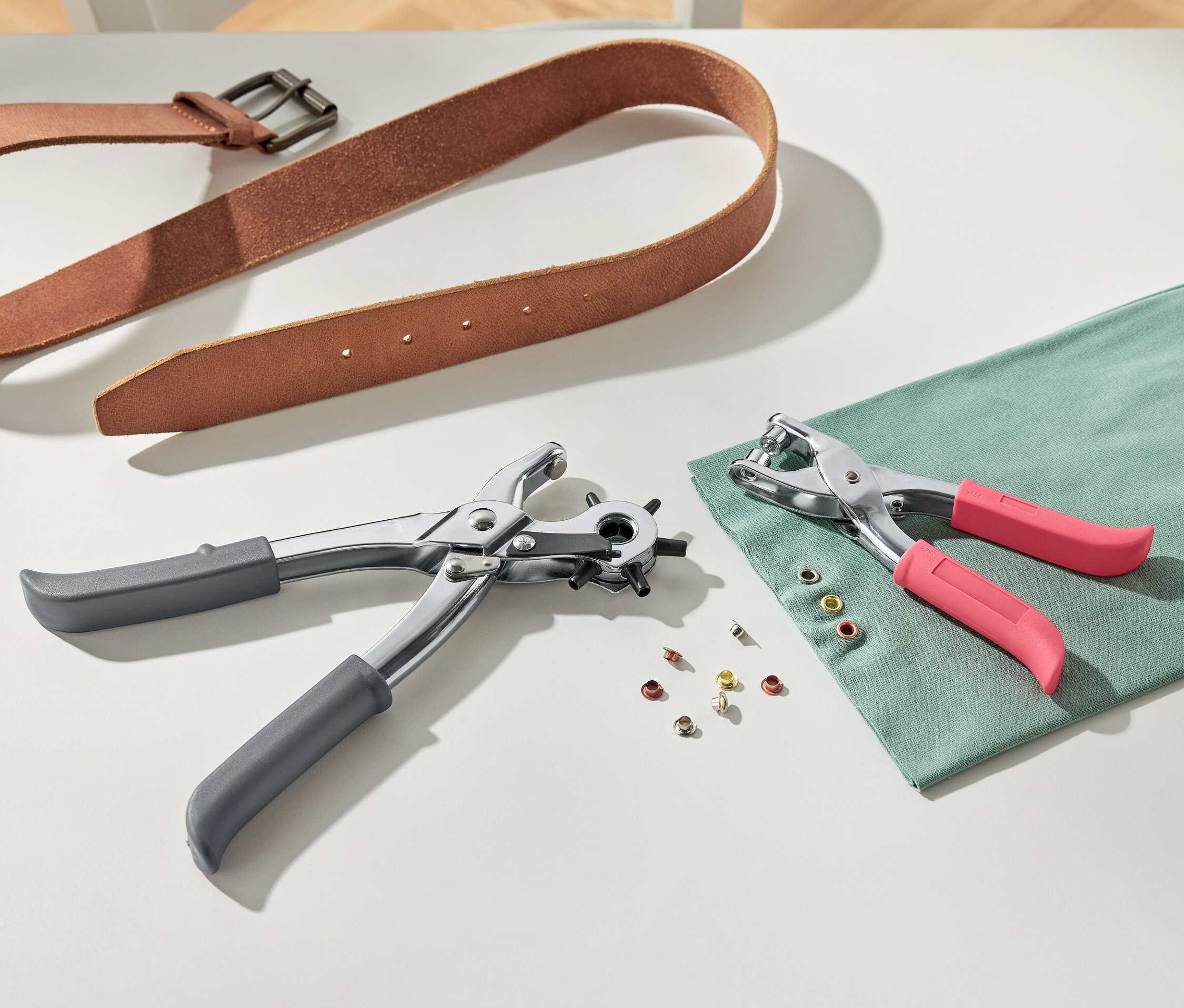 Ein brauner Ledergürtel und eine Loch- und Nietenzange auf einem weißen Hintergrund.