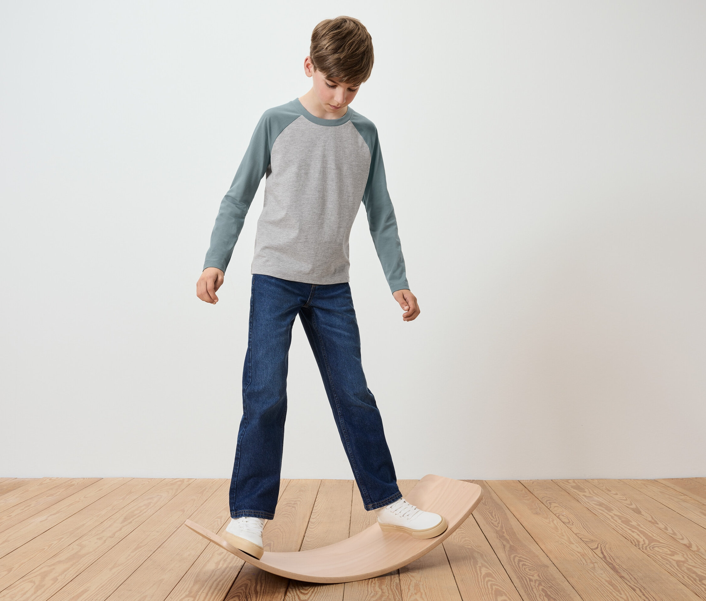 Junge steht auf einem hölzernen Balance Board, trägt ein graues T-Shirt und Jeans.