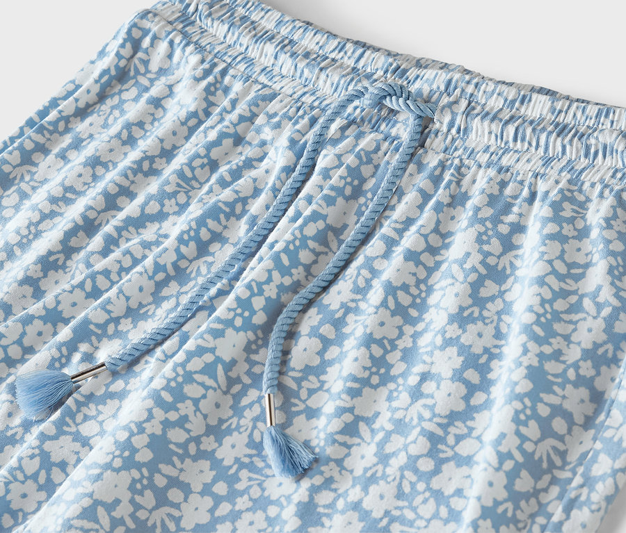 Detail einer hellblauen Hose mit weißem Blumendruck, elastischem Bund und blauem Kordelzug.