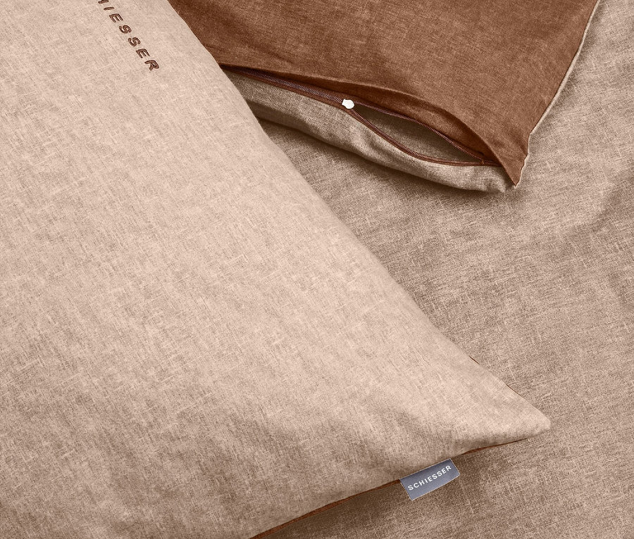 Detailaufnahme einer beigen Bettwäsche und eines braunen Kissens.