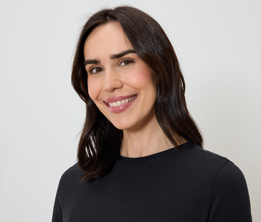 Porträt einer lächelnden Frau mit langen, braunen Haaren in einem schwarzen T-Shirt.