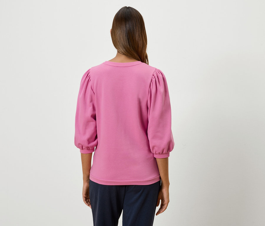 Frau steht mit dem Rücken und trägt ein pinkfarbenes Sweatshirt mit Dreiviertel-Puffärmeln.