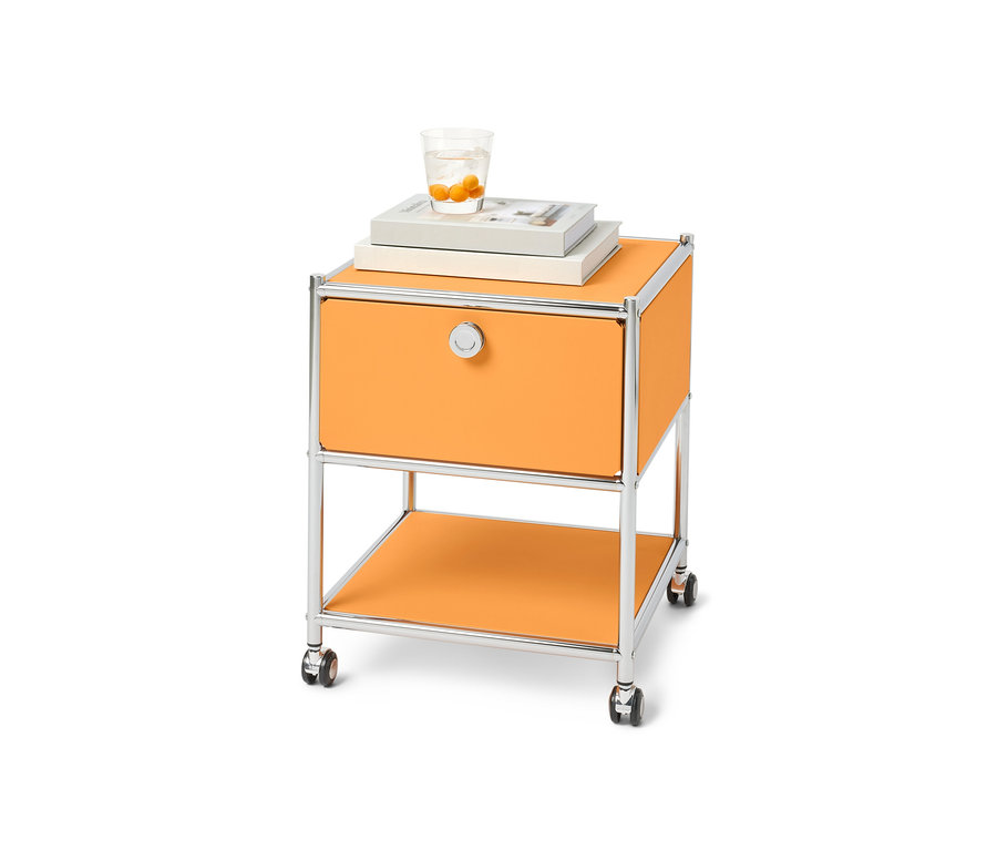 Ein orangefarbener Beistelltisch mit Schublade Metall »CN3« auf Rollen. Auf dem Tisch liegen Bücher und ein Glas Wasser.