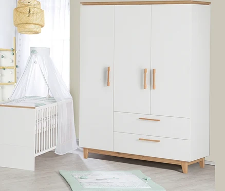 Ein Kinderzimmer mit einem weißen Kinderbett mit Himmel, einem weißen dreitürigen Kleiderschrank und einer Spieldecke auf dem Boden.
