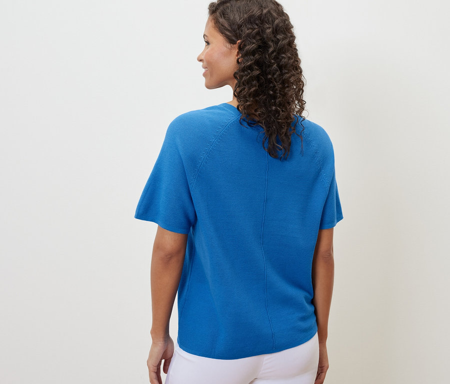 Eine Frau von hinten, mit einem kobaltblauen Feinstrick-Shirt und weissen Hosen.