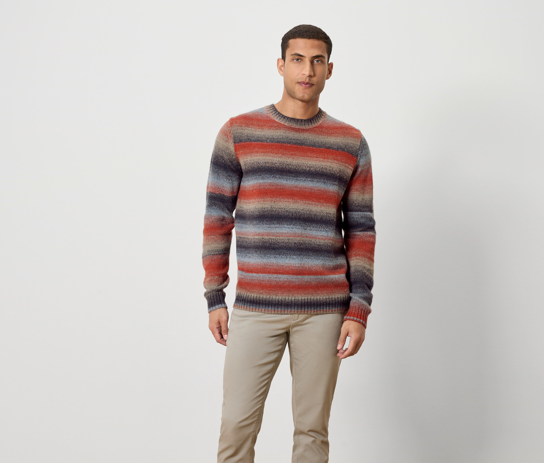 Ein Mann steht und trägt einen gestreiften Pullover und Hose.