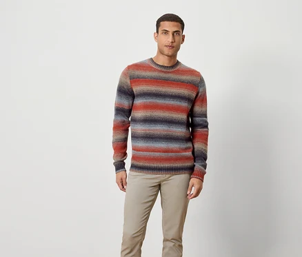 Ein Mann steht und trägt einen gestreiften Pullover und Hose.