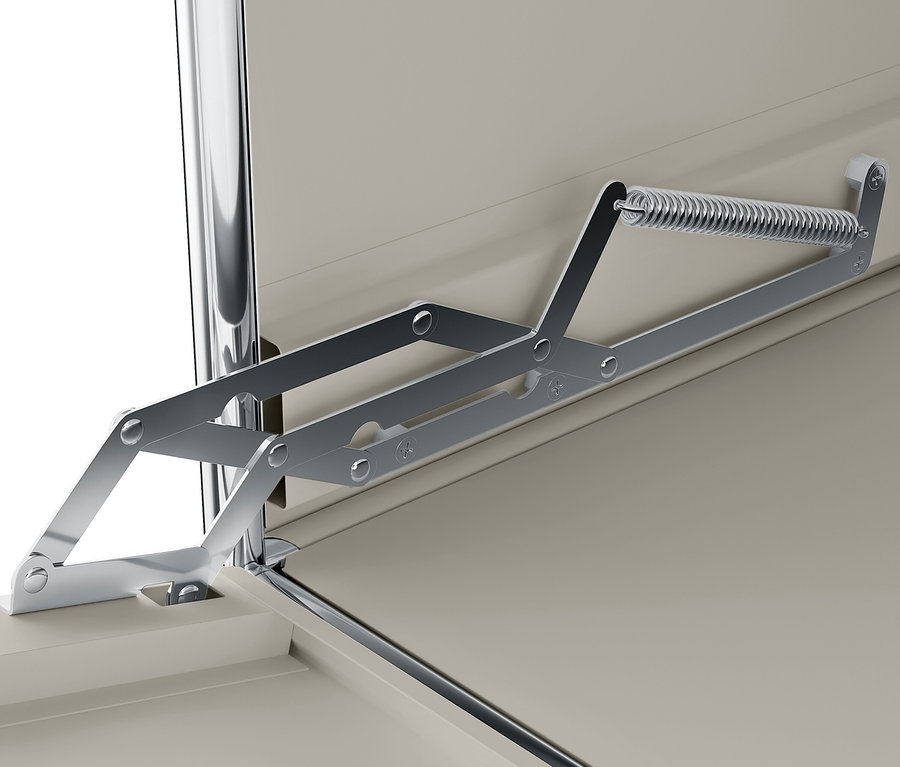 Detail eines silbernen Mechanismus mit Feder, der an einem beigen Schrank befestigt ist.