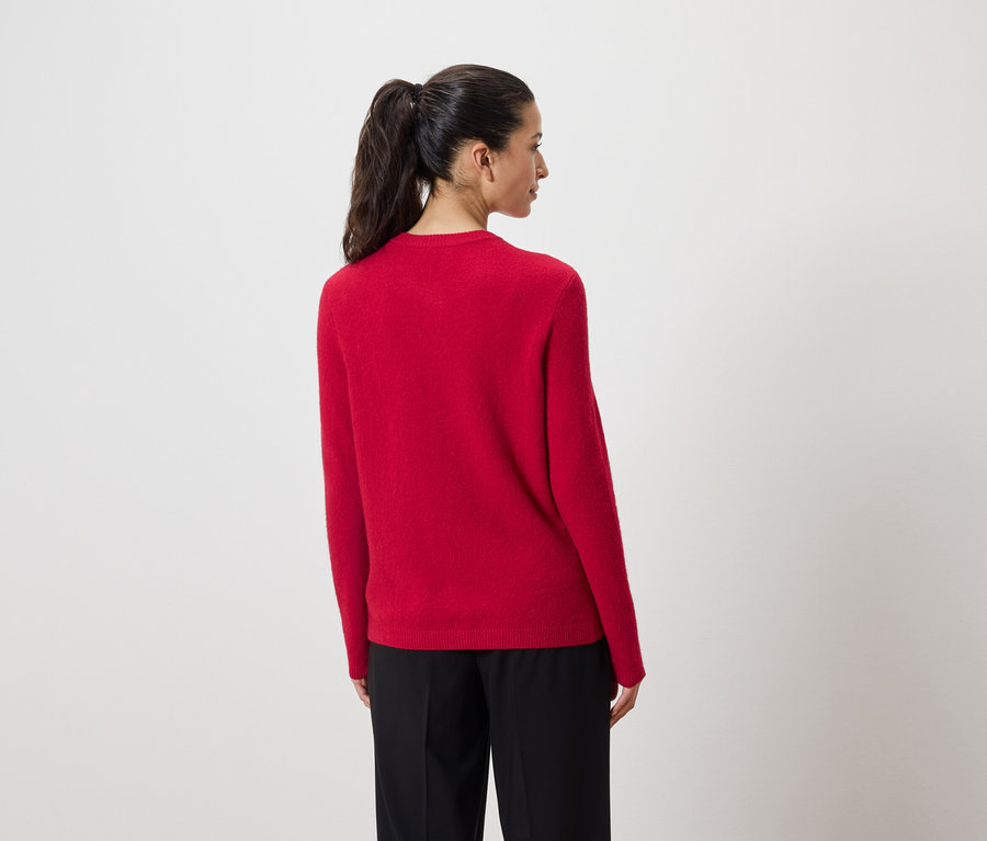 Frau mit dem Rücken zur Kamera trägt einen roten Pullover und eine schwarze Hose.