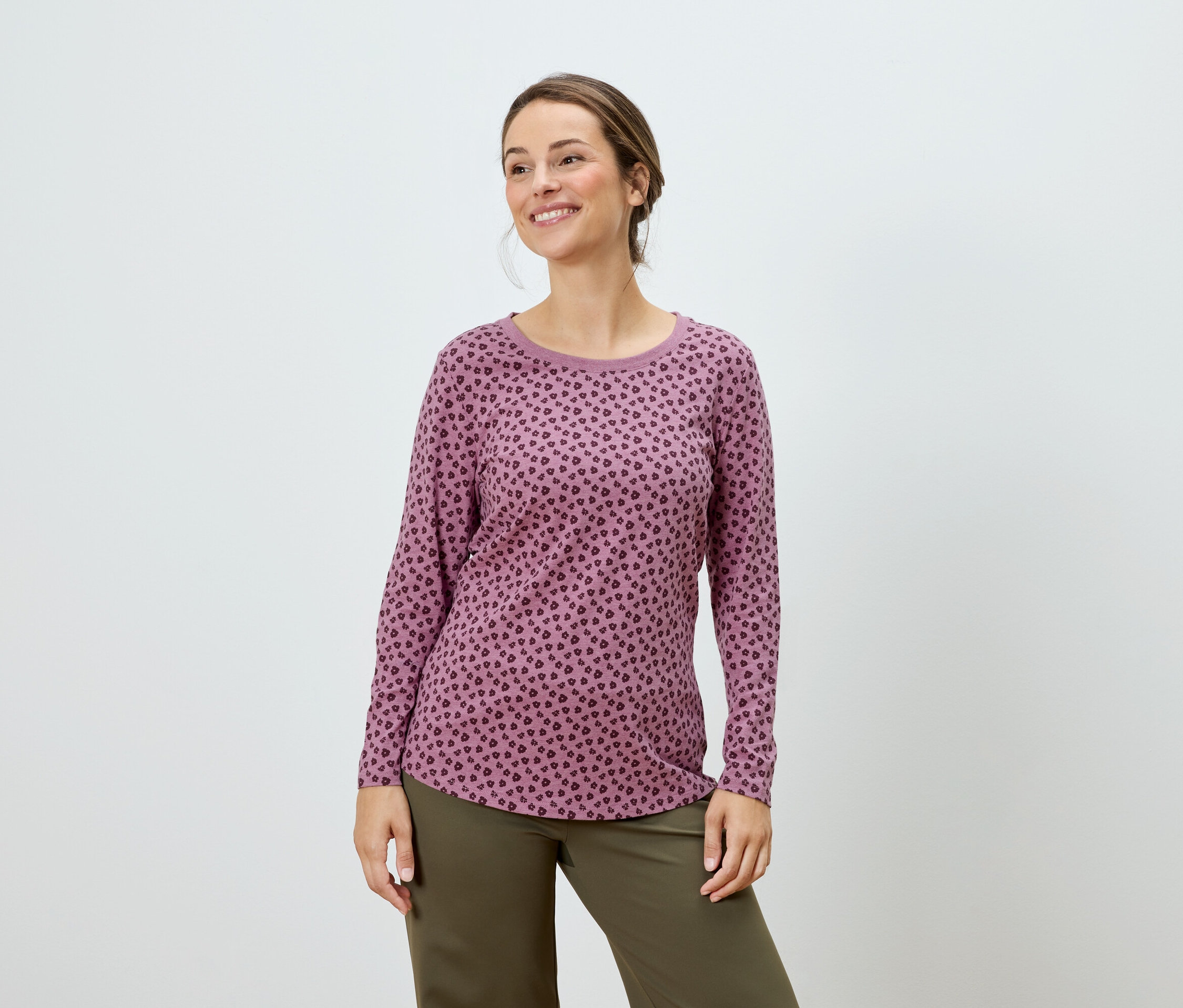 Frau posiert in einem rosafarbenen Langarmshirt mit Punktmuster und grüner Hose.