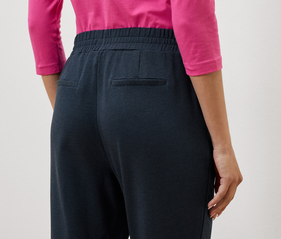 Nahaufnahme der Rückseite einer Frau, die eine dunkelblaue Hose und ein pinkes Oberteil trägt.