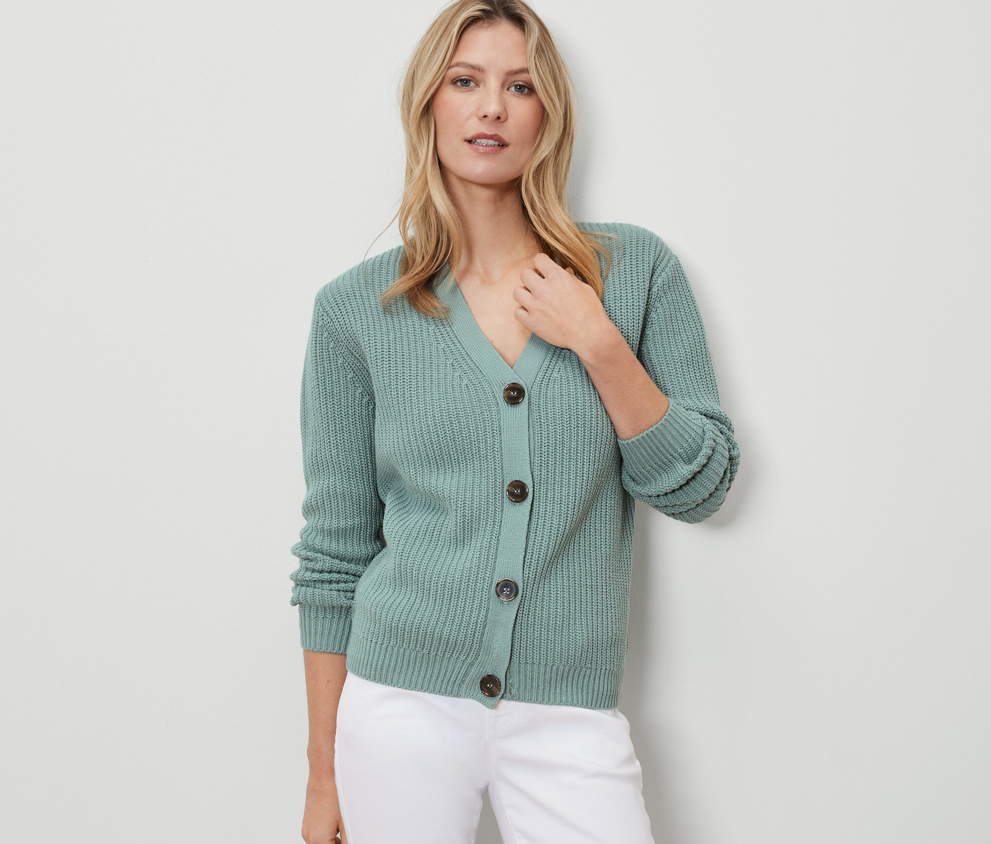 Frau trägt einen Grobstrick-Cardigan in Salbei und weiße Hosen.