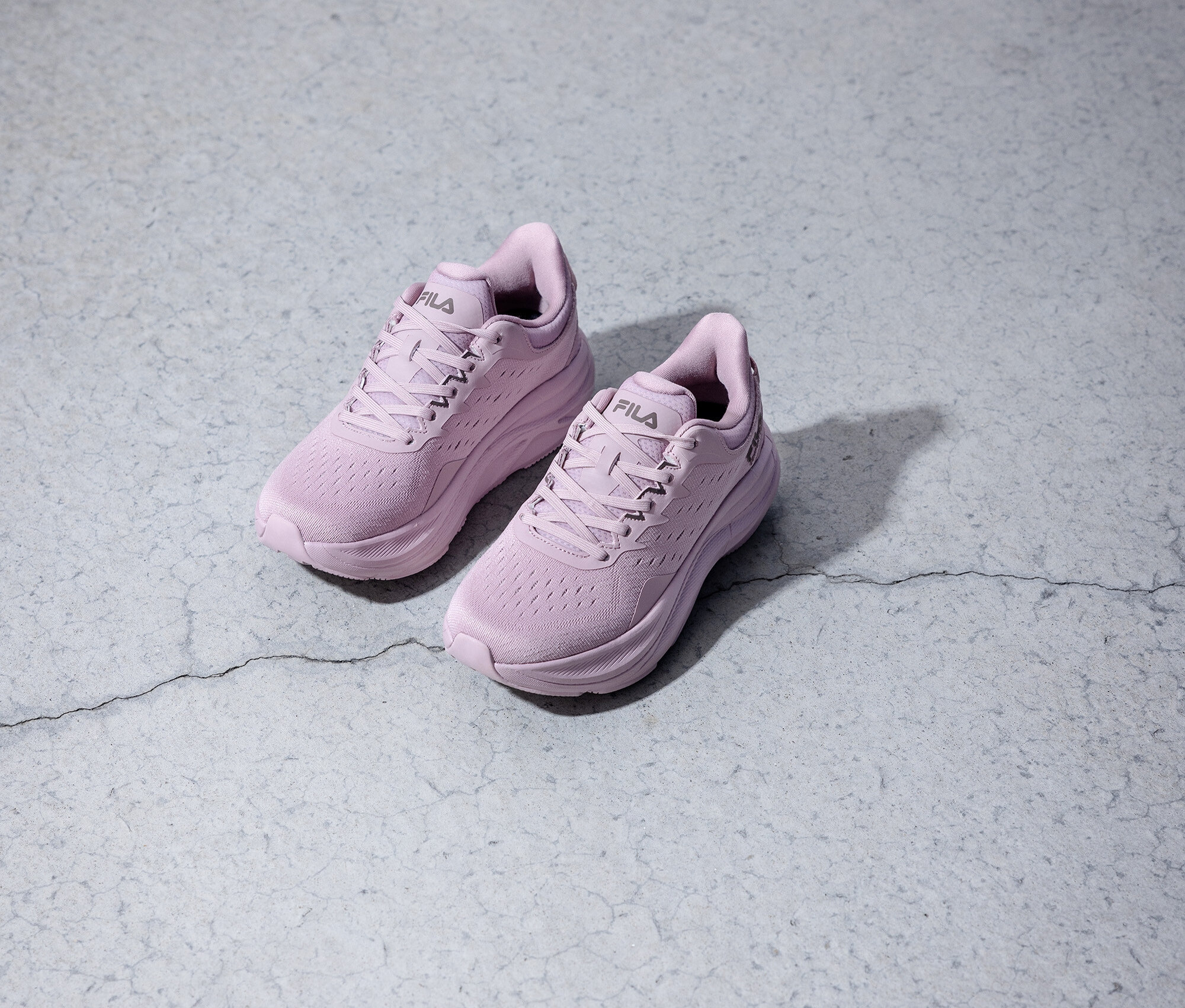 Zwei lilafarbene Fila-Laufschuhe stehen auf einem grauen Untergrund.