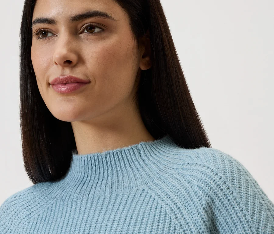Nahaufnahme einer Frau mit langen, dunklen Haaren, die einen hellblauen Strickpullover trägt.