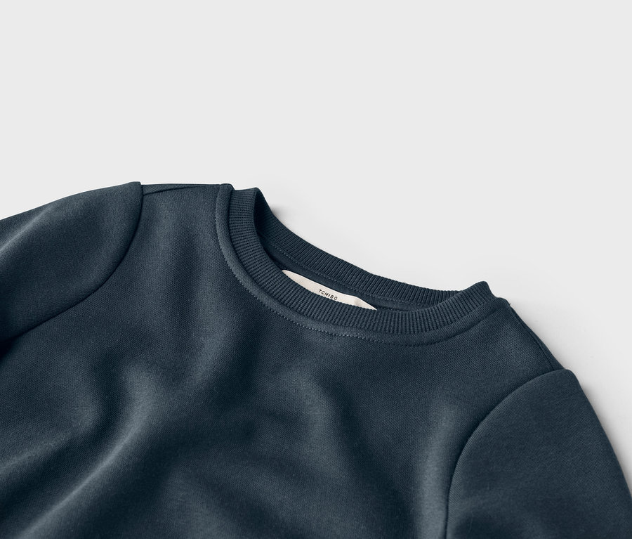 Detailansicht eines marineblauen Sweatshirts mit Rundhalsausschnitt und einem Etikett der Marke Tchibo am Kragen.