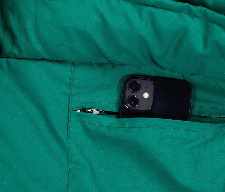 Nahaufnahme einer grünen Jacke mit einem schwarzen Smartphone in der Reißverschlusstasche.