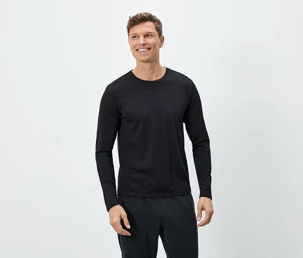 Ein lächelnder Mann trägt ein schwarzes Langarmshirt und eine schwarze Hose vor einem weißen Hintergrund.