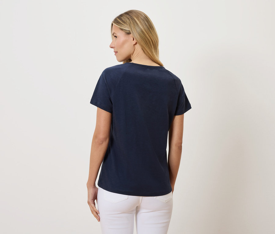 Rückansicht einer Frau mit blonden Haaren, die ein marineblaues T-Shirt und weiße Jeans trägt.
