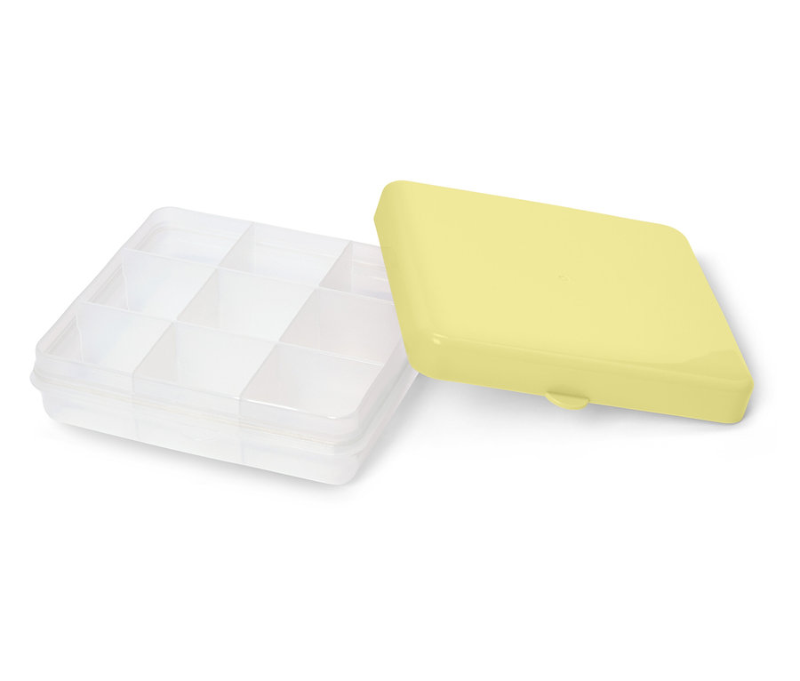 Eine durchsichtige Aufbewahrungsbox mit Fächern und einem gelben Deckel liegt daneben.